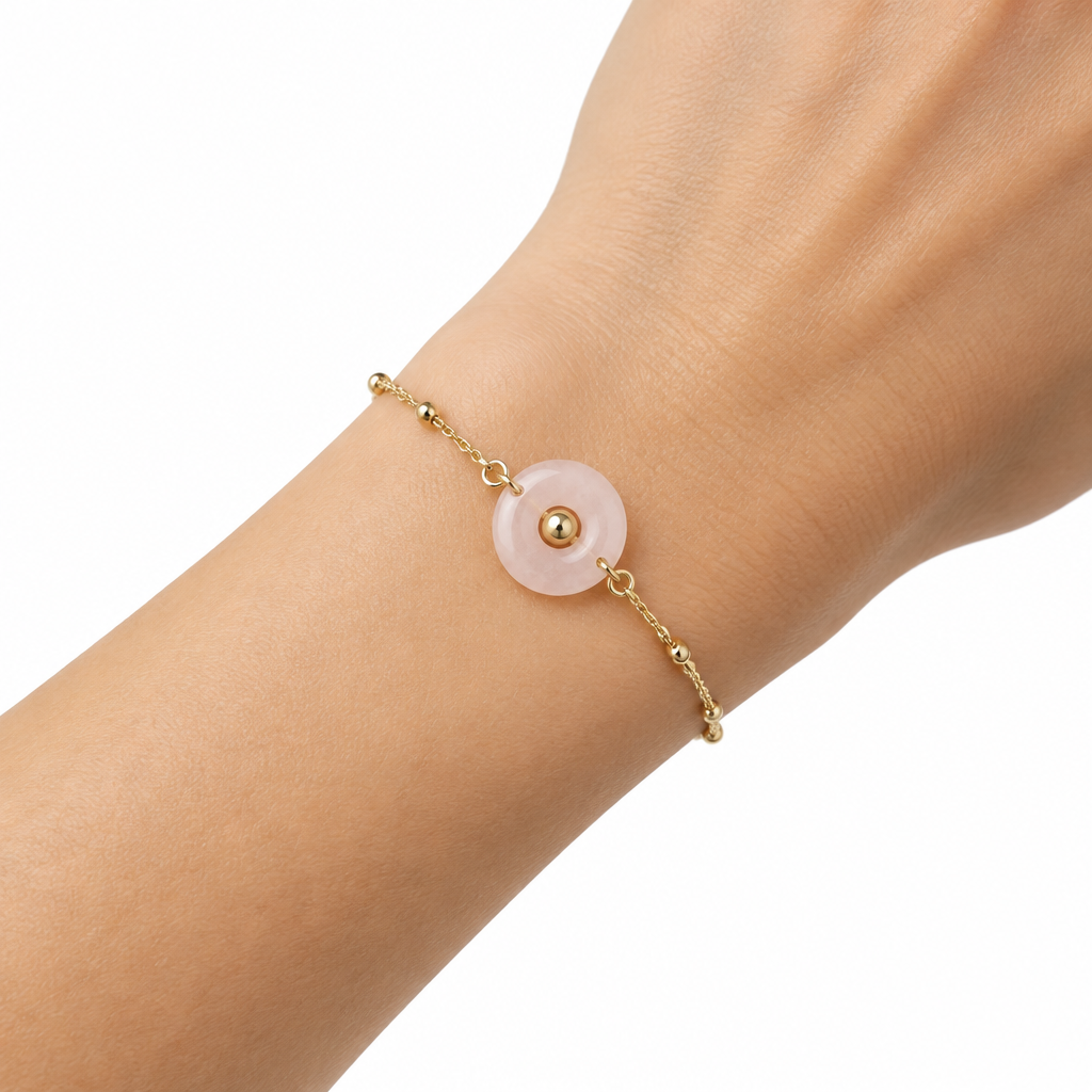 Delikatna bransoletka z rozowym kamieniem na nadgarstku modelki, biale tlo