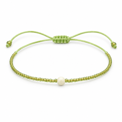 Jasnozielona cienka bransoletka boho z kremowym koralikiem, produkt na bialym tle